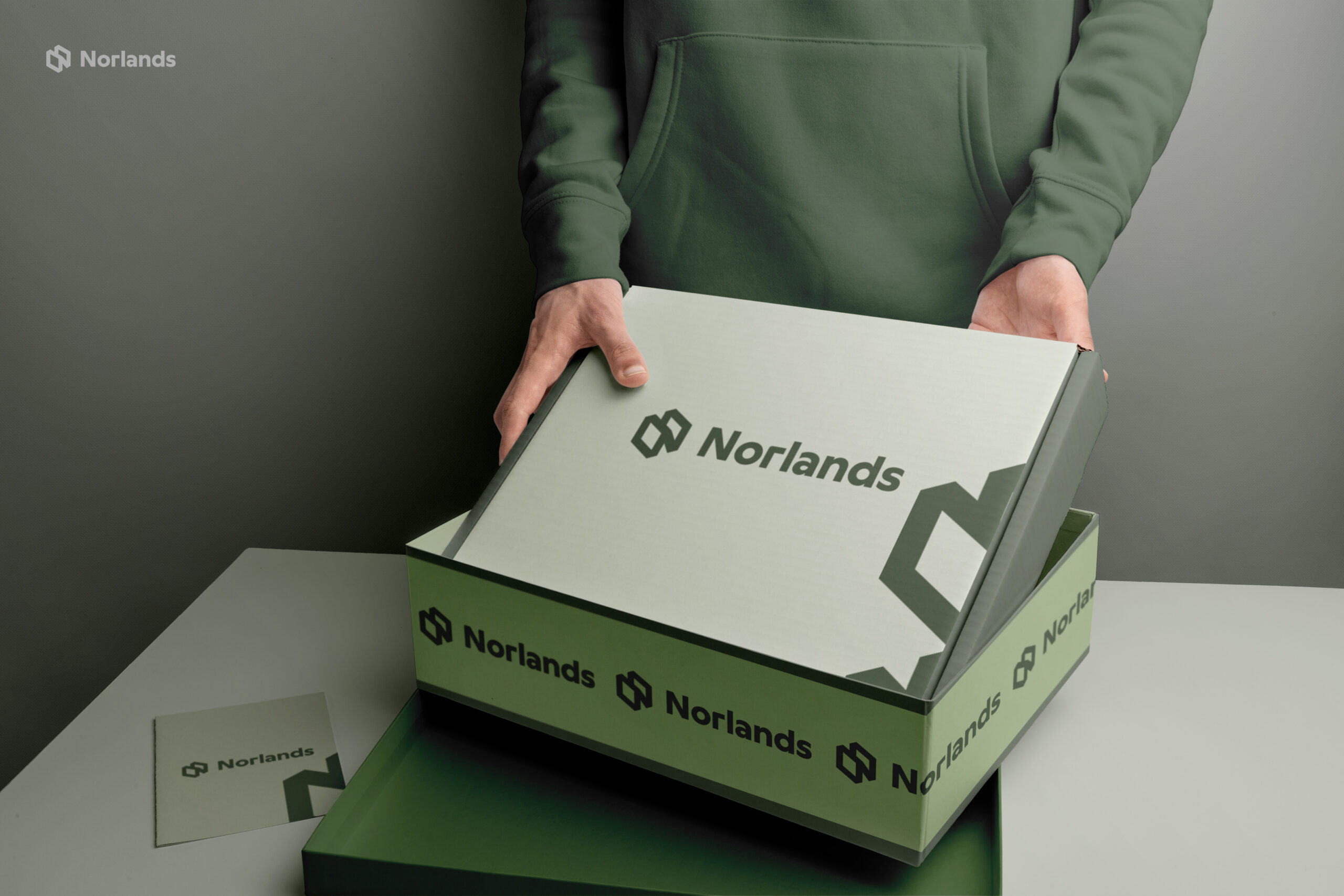 custom boxes in Canada A person in a green hoodie opens a sleek green NORLANDS box with a modern logo design in a softly lit setting.